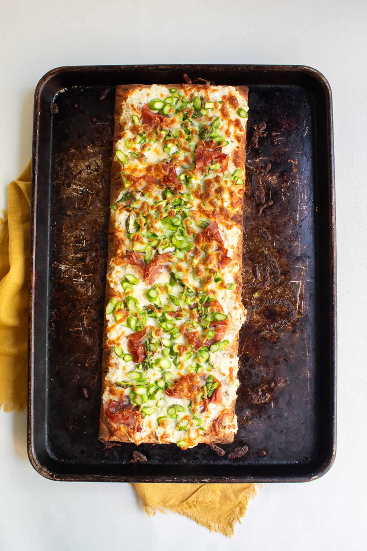 The baked pizza has golden cheese, crisp prosciutto, and bright green asparagus.