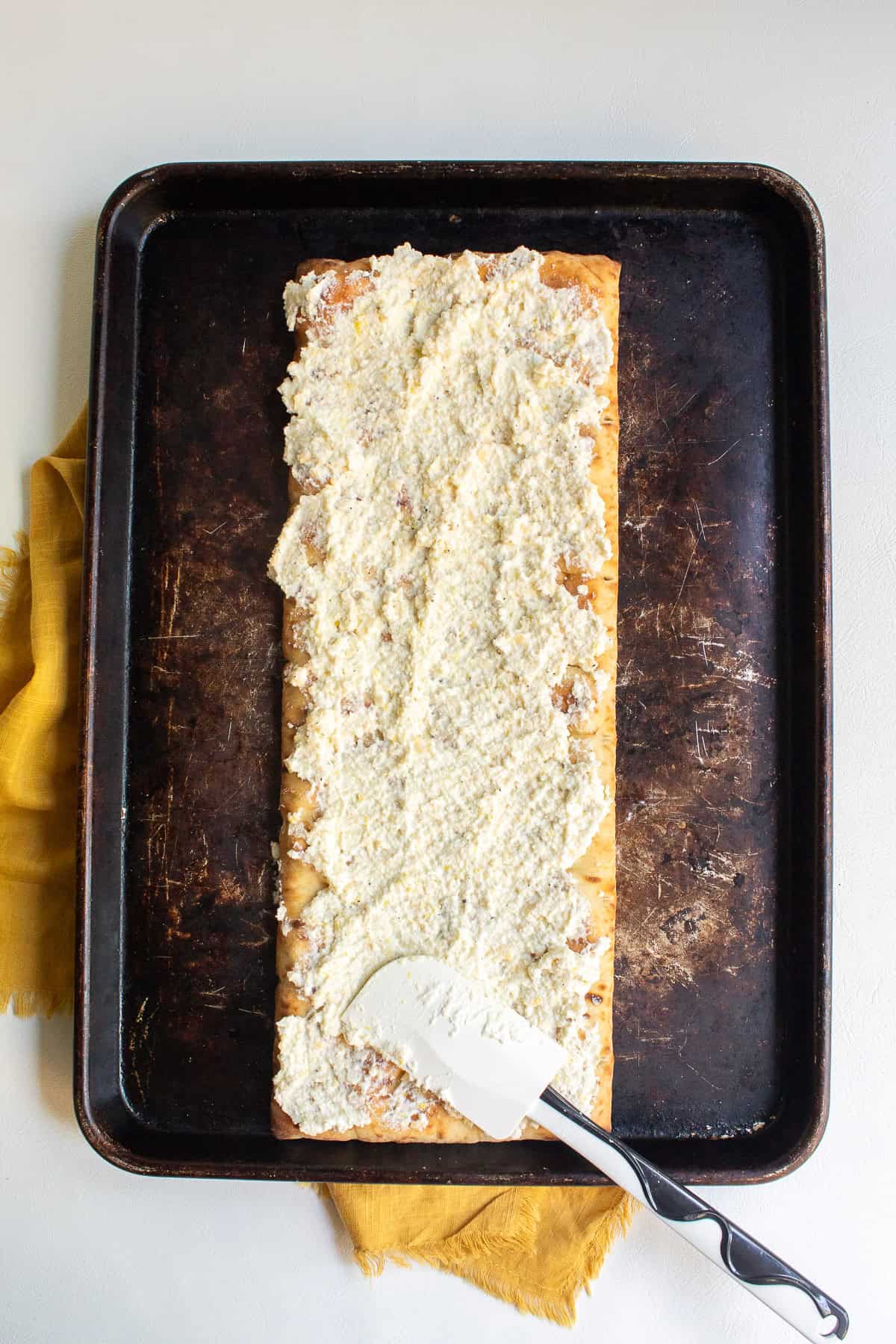 The ricotta mixture is spread over the pizza crust using a silicone spatula.