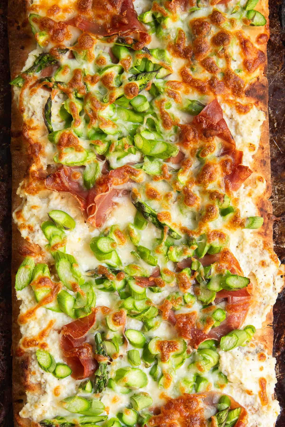 A detailed image of the pizza shows golden cheese, crisp prosciutto, and bright green asparagus.
