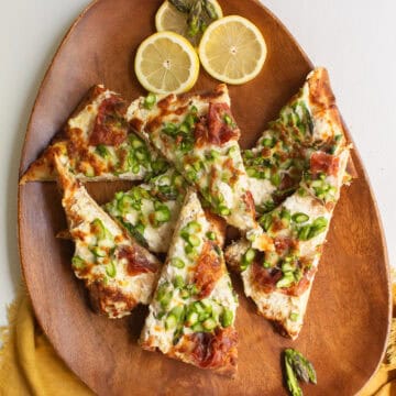 Slices of asparagus pizza are piled on a wooden platter.