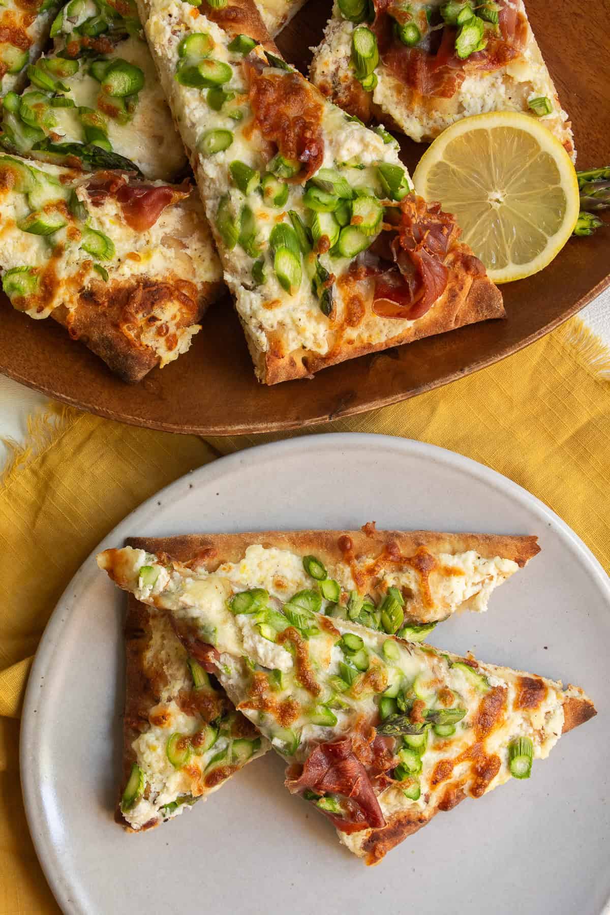 The pizza is served on a plate next to a platter of pizza garnished with lemon slices.