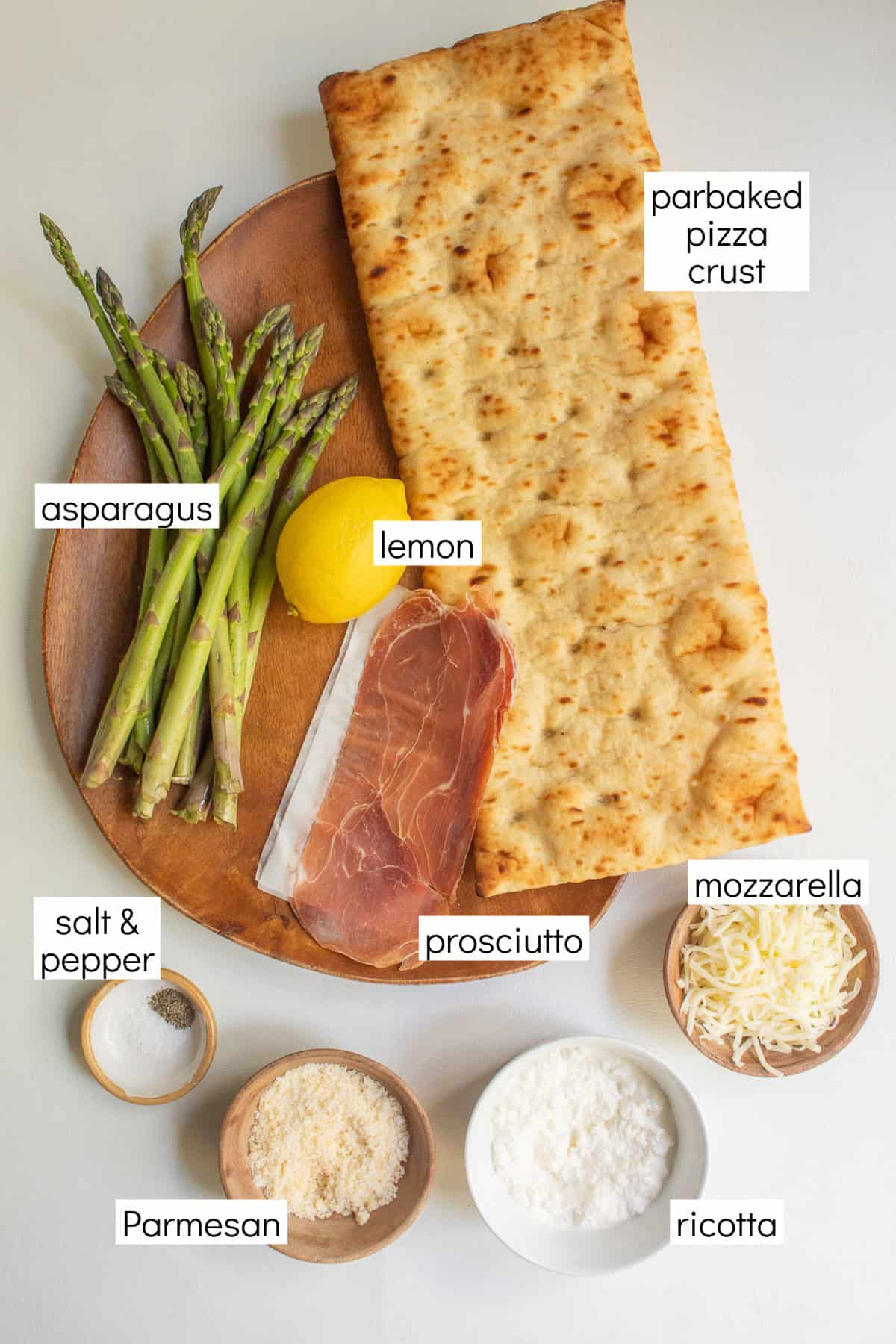 Ingredients for the recipe are displayed and labeled with white text boxes including the words parbaked pizza crust, asparagus, lemon, salt & pepper, prosciutto, mozzarella, Parmesan, and ricotta.