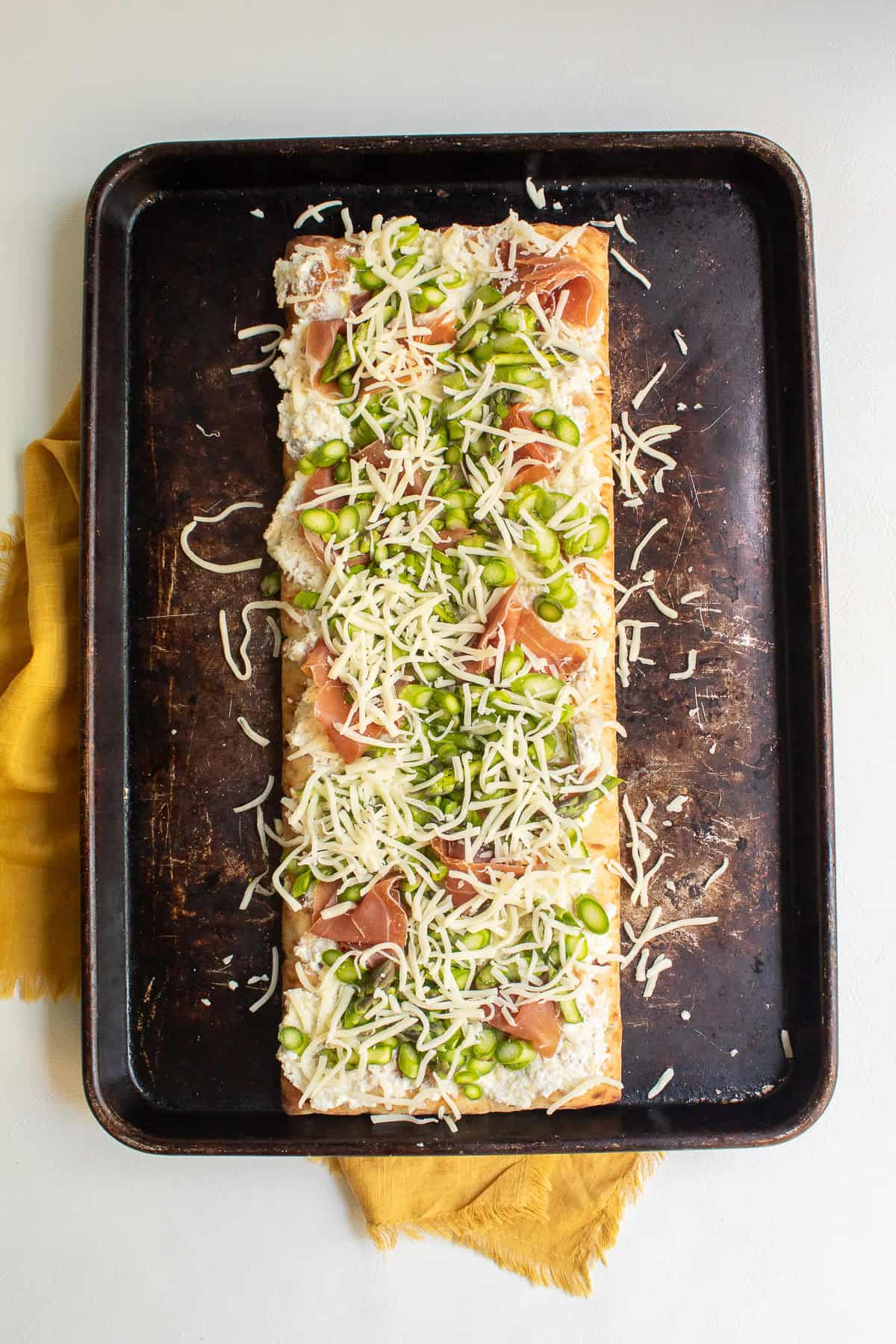 Mozzarella cheese is sprinkled over the top of the pizza before baking.