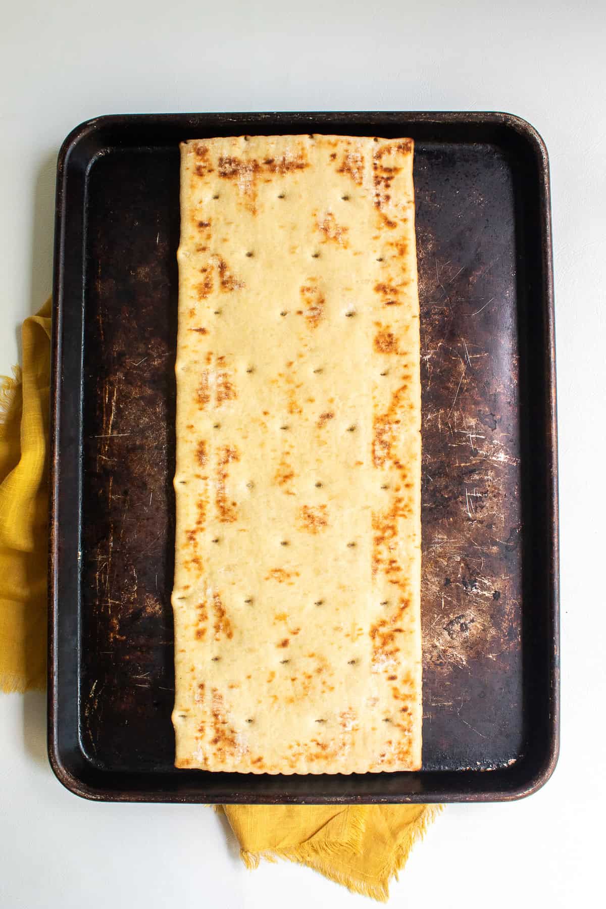 The underside of the pizza crust is face up on a dark brown sheet pan.