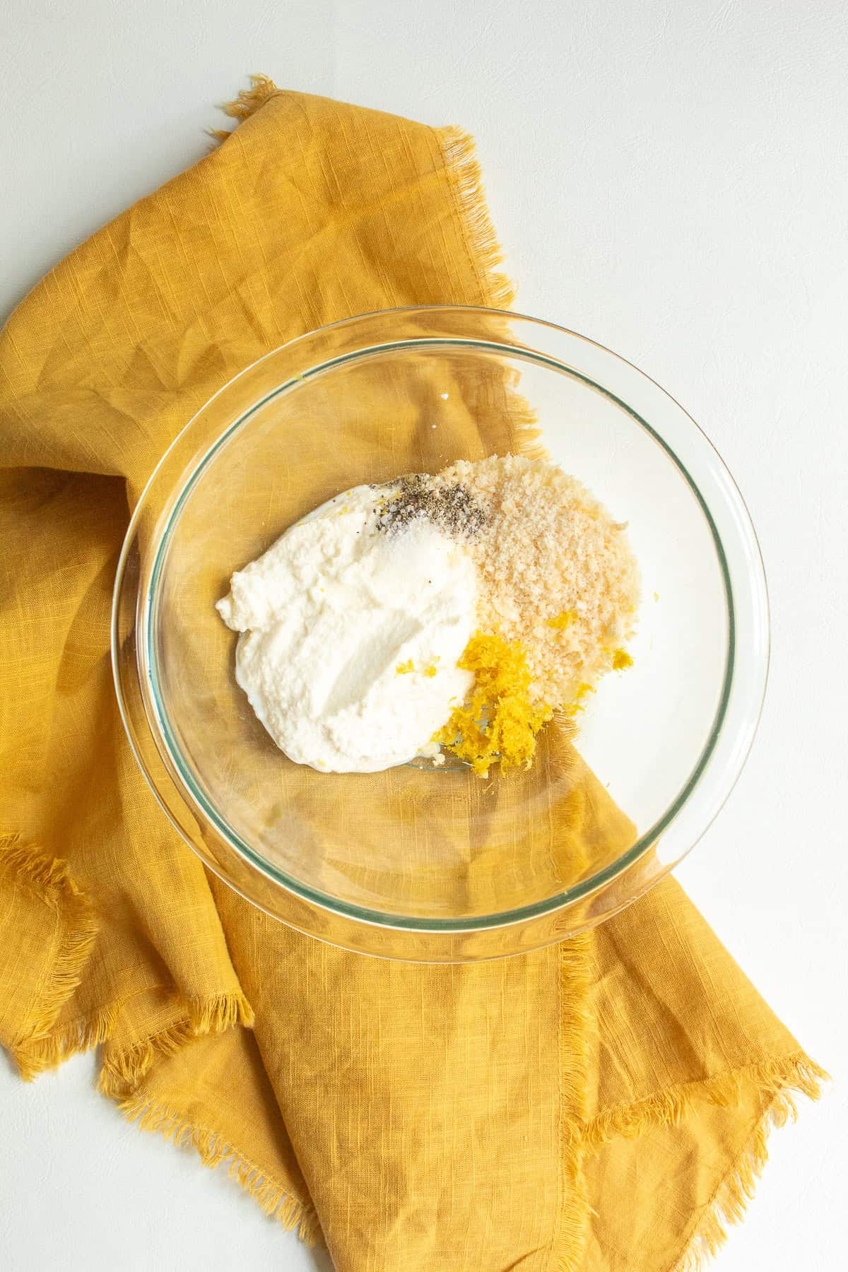 Ricotta, salt, pepper, Parmesan cheese, and fresh lemon zest are added to a medium glass bowl.