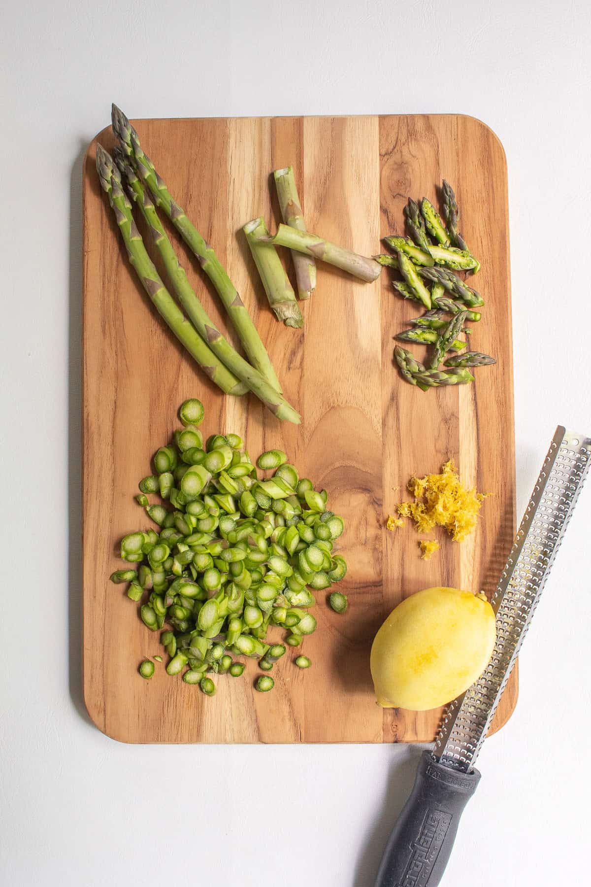 The asparagus and lemon are prepared for the pizza on a wooden cutting board.