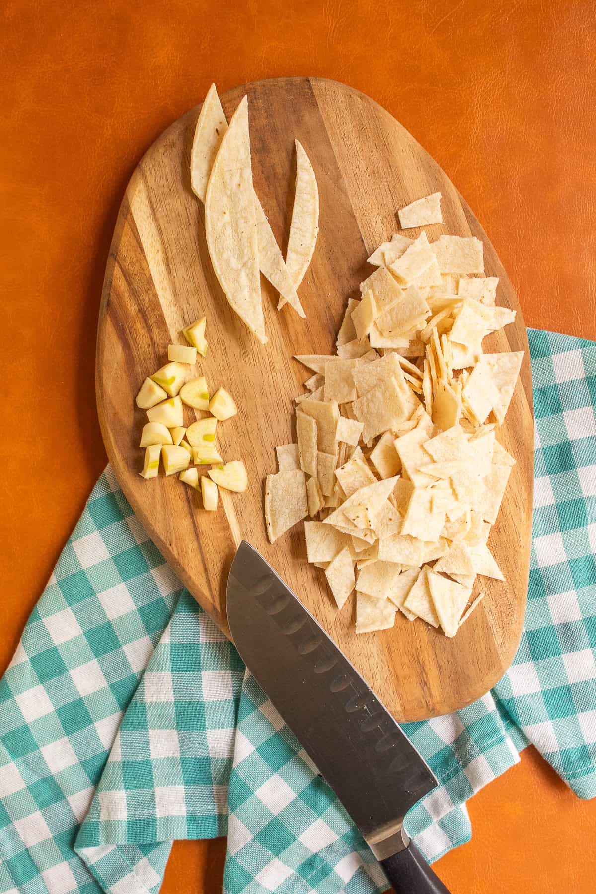 Corn tortillas are roughly chopped alongside some garlic.