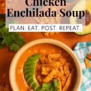 Avocado slices are fanned out over the top of a bowl of soup along with crisp tortilla strips and cilantro leaves. A white text box at the top of the image contains the words, "creamy chicken enchilada soup" and "plan. eat. post. repeat."