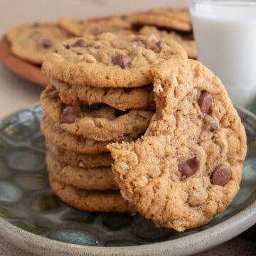 One bite is missing from a golden brown cookie studded with chocolate chips and leaning on a stack of six more cookies.