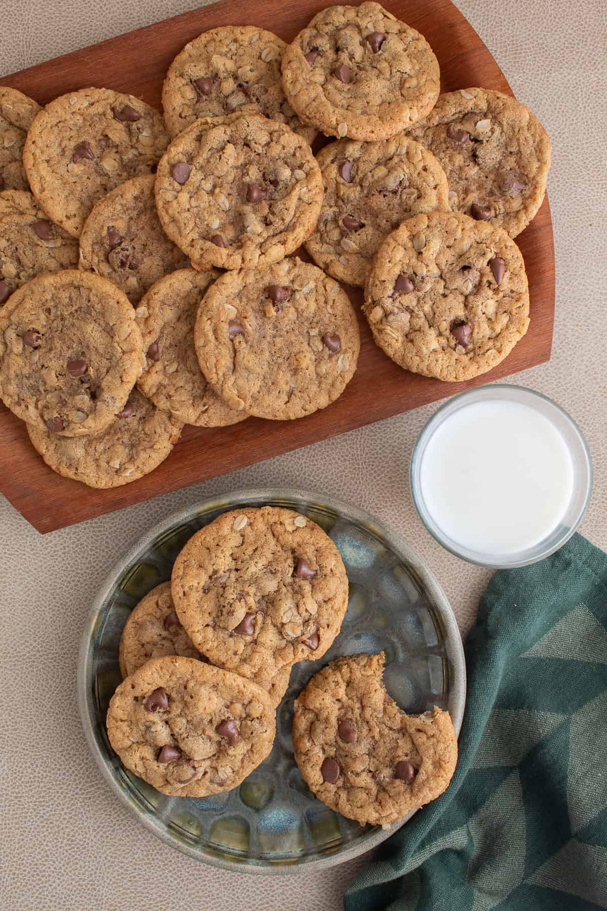 A plate of cookies, a glass of milk, and a wooden platter sit on a brown surface.