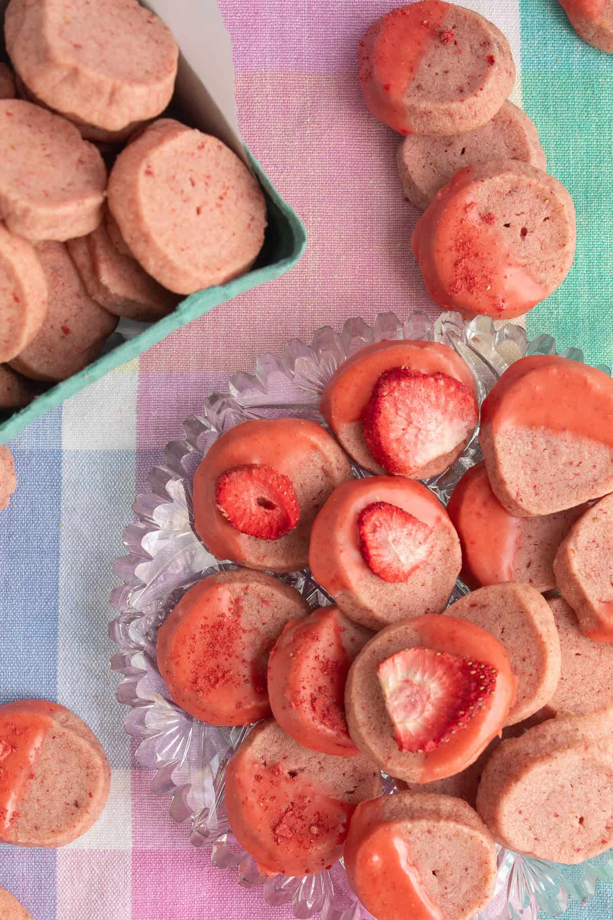 A glass platter of cookies is decorated with dried strawberries, strawberry glaze, and crushed strawberry powder.