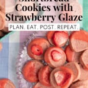 A glass platter of cookies is decorated with dried strawberries, strawberry glaze, and crushed strawberry powder. A white text box at the top of the image contains the words, "strawberry shortbread cookies with strawberry glaze." and "plan, eat, post. repeat."