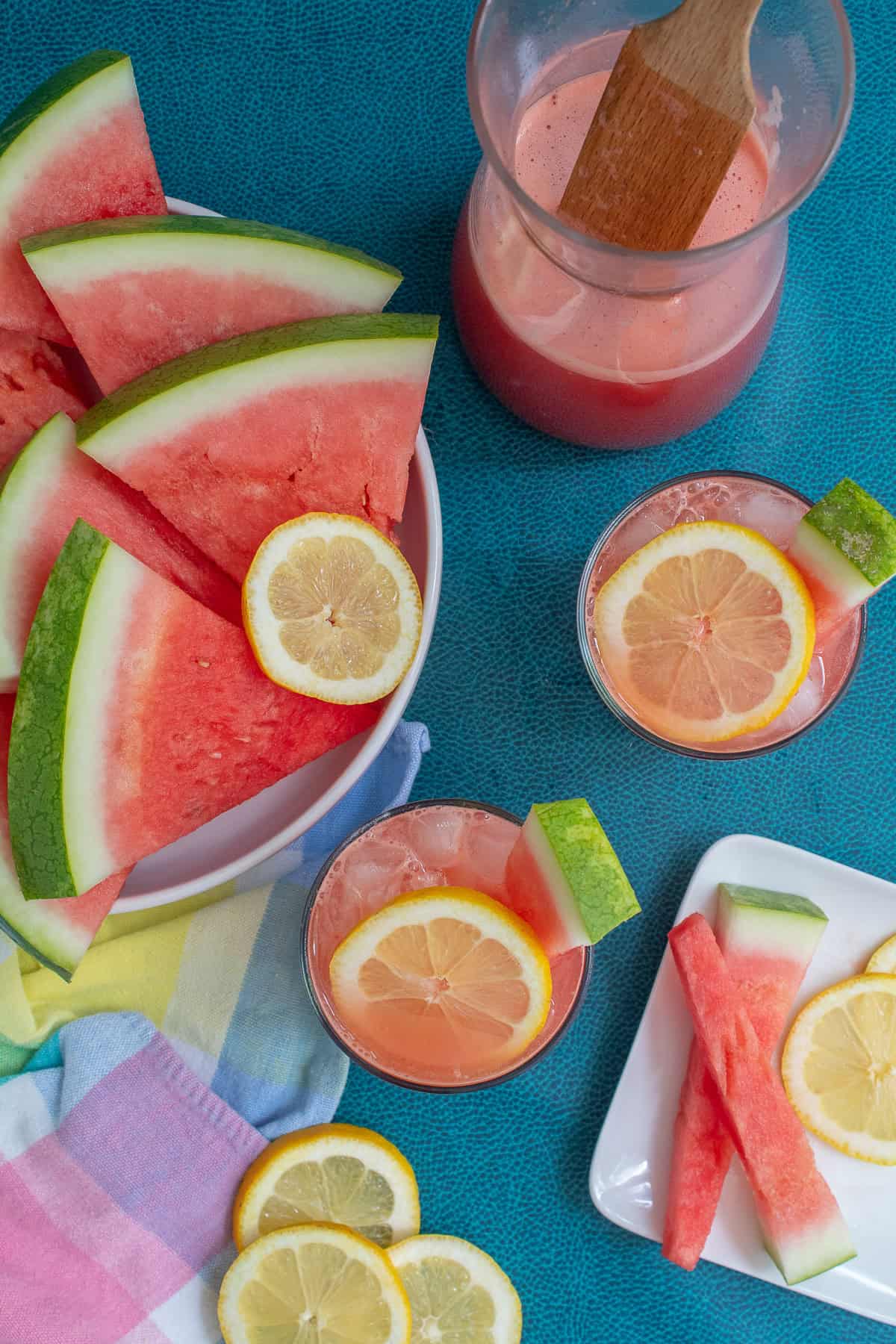 Glasses of watermelon lemonade are garnished with lemon wheels and watermelon spears.