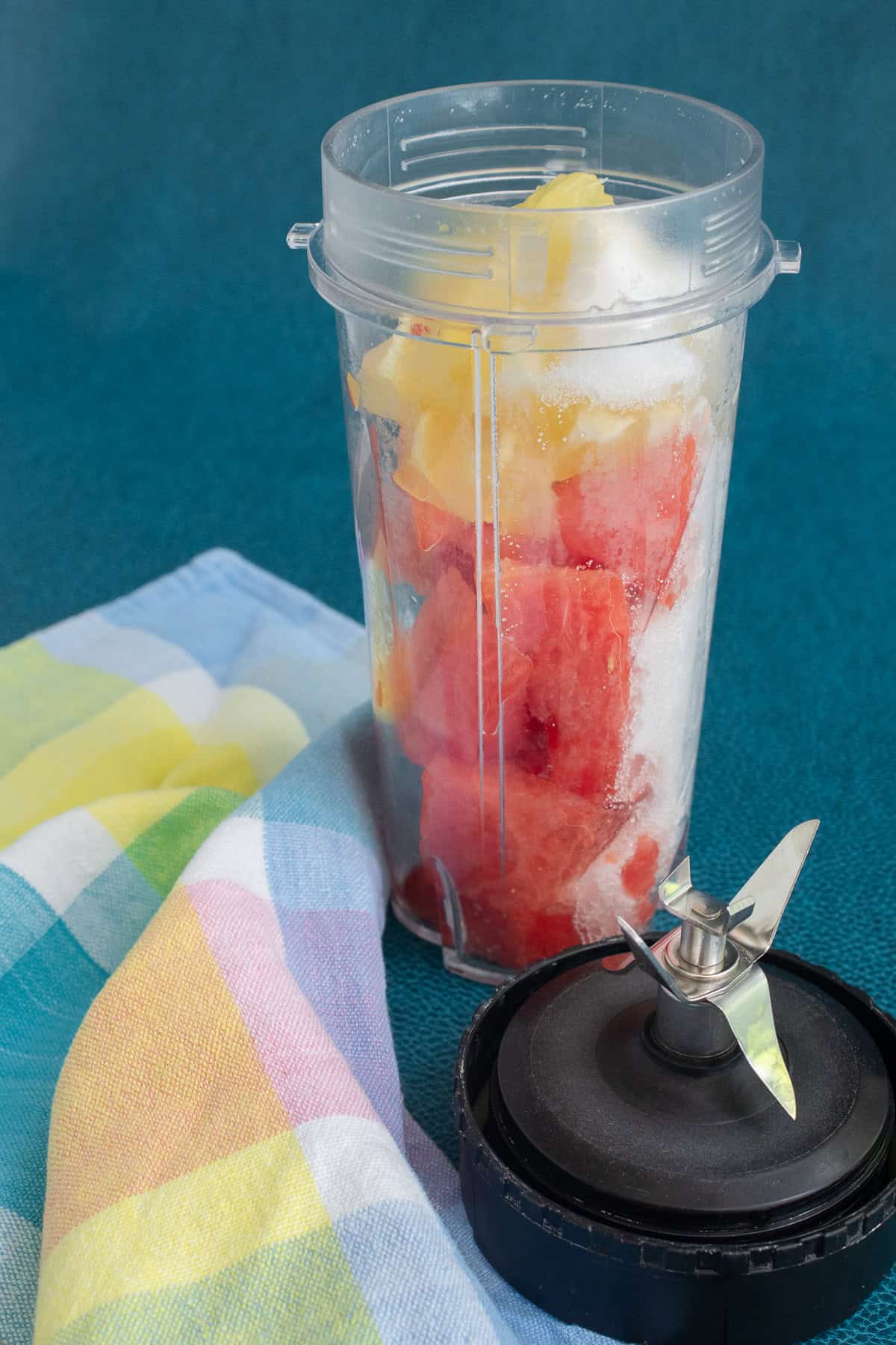 Watermelon chunks, sugar, and whole lemon are added to a mini blender.