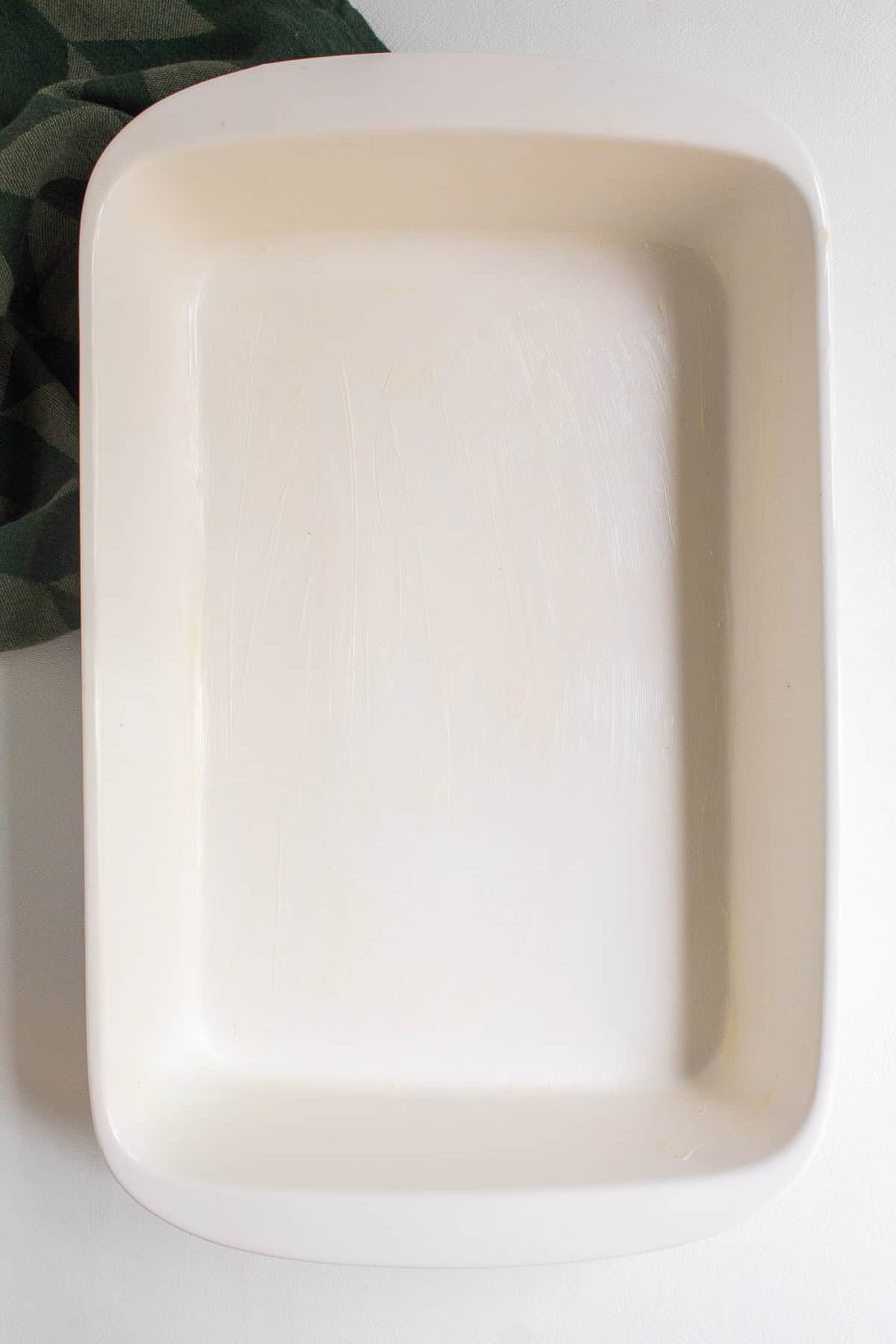 A white 9 x 13 casserole dish is greased in preparation for the baked gnocchi.