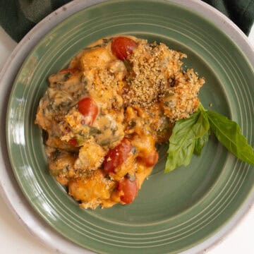 A green plate is loaded with baked gnocchi with breadcrumbs, grape tomatoes, basil, and spinach visible in the sun dried tomato sauce.