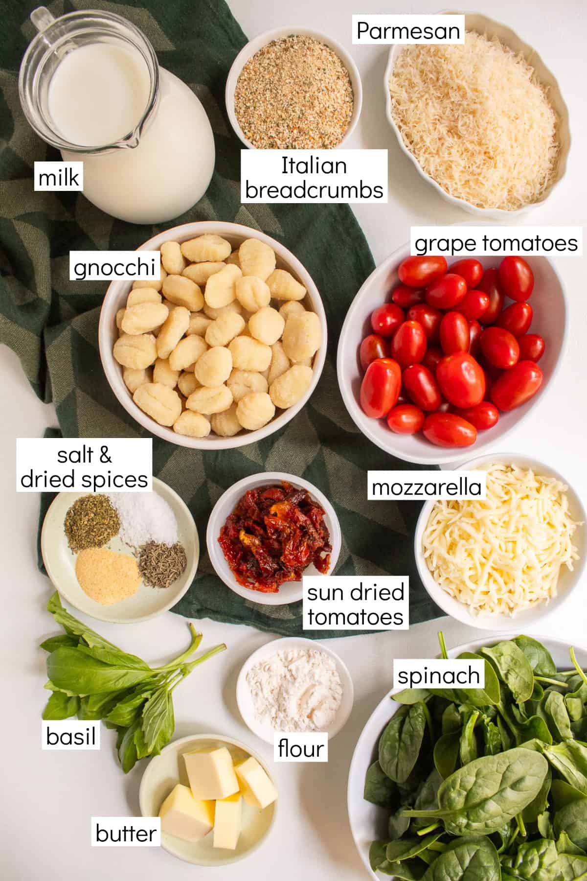 Ingredients for the recipe are displayed and labeled with white text boxes including the words milk, Italian breadcrumbs, Parmesan, gnocchi, grape tomatoes, salt & dried spices, sun dried tomatoes, mozzarella, basil, flour, butter, and spinach.