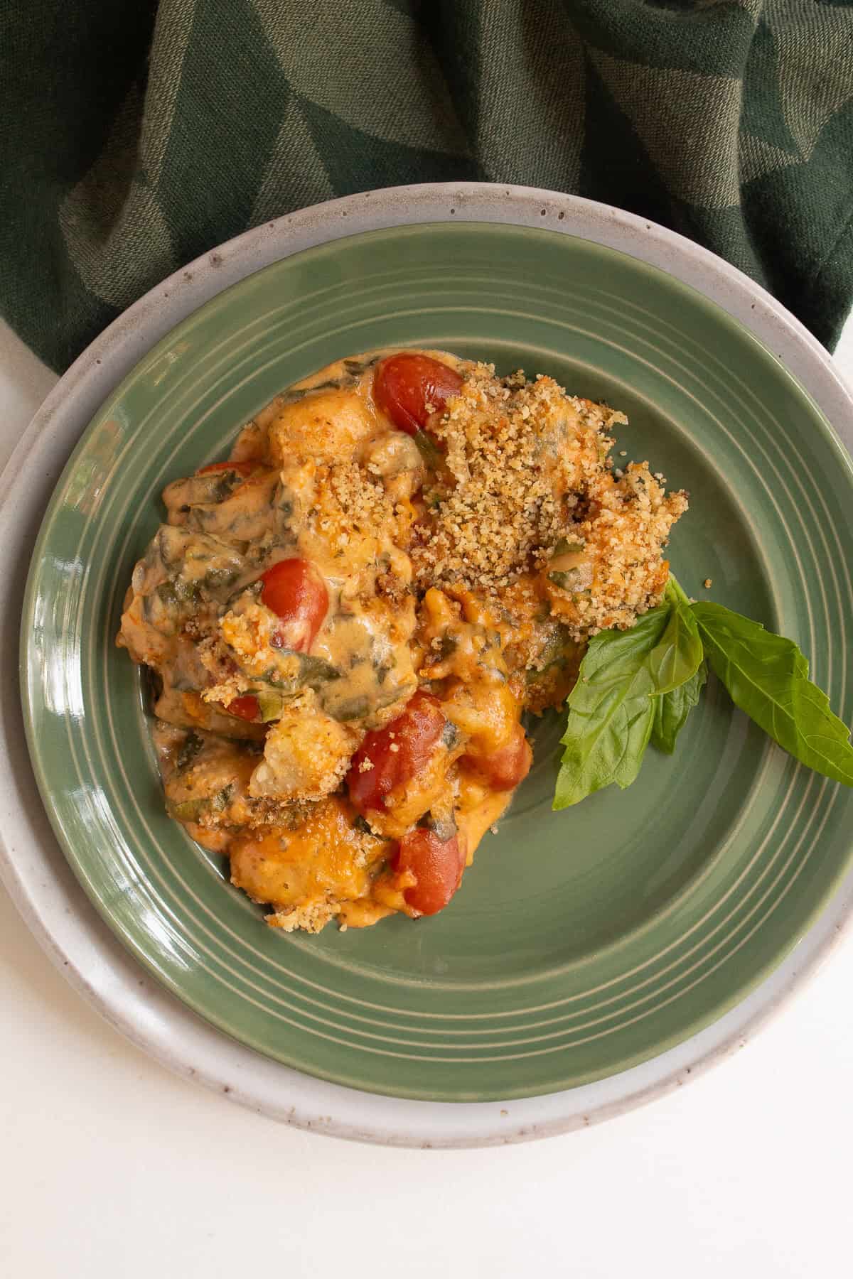 A green plate is loaded with baked gnocchi with and a basil garnish.