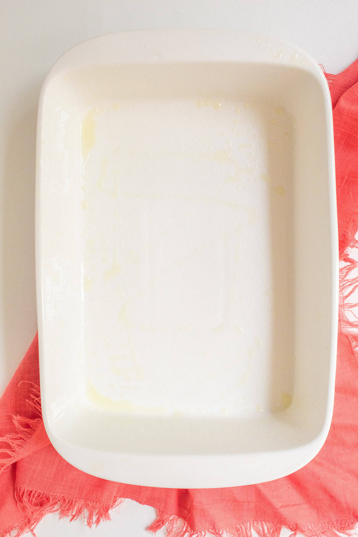 A white baking dish is coated with cooking spray.