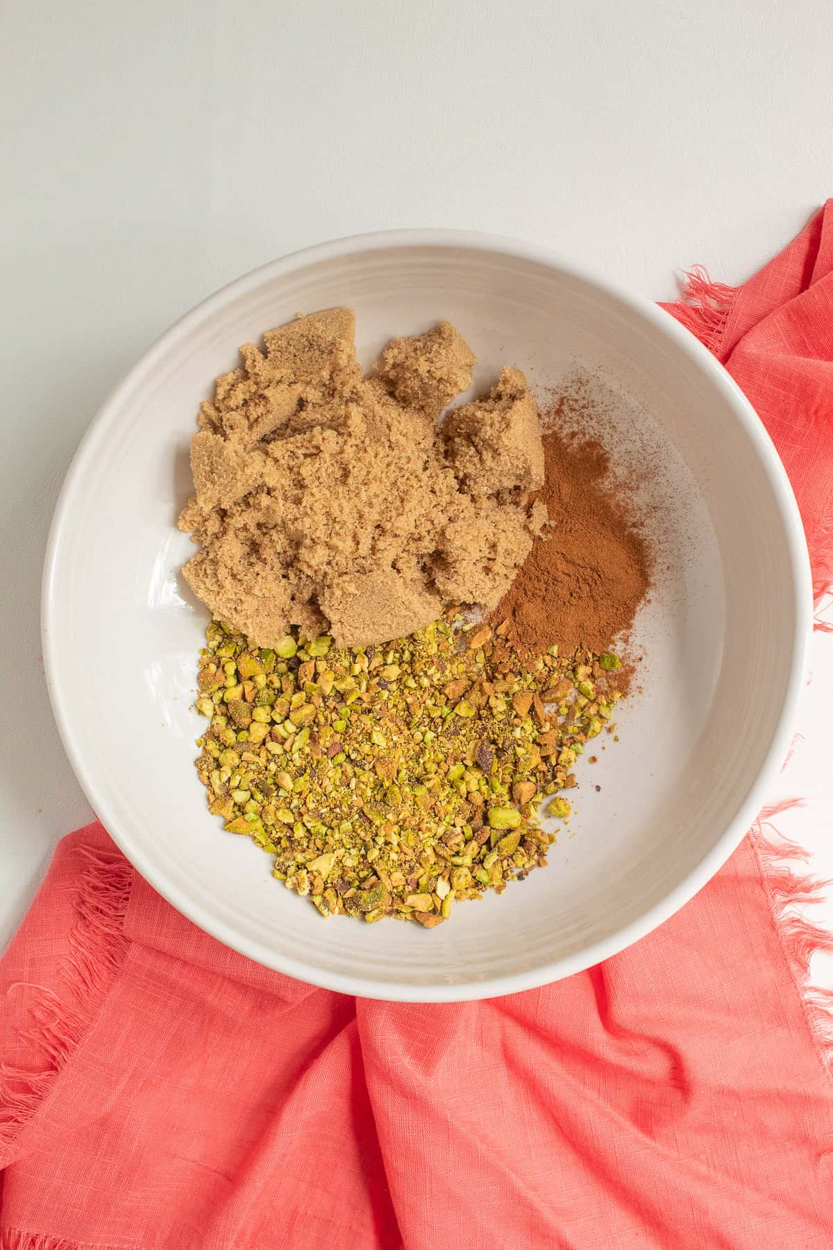 Chopped pistachios, brown sugar, and cinnamon are added to a white bowl.