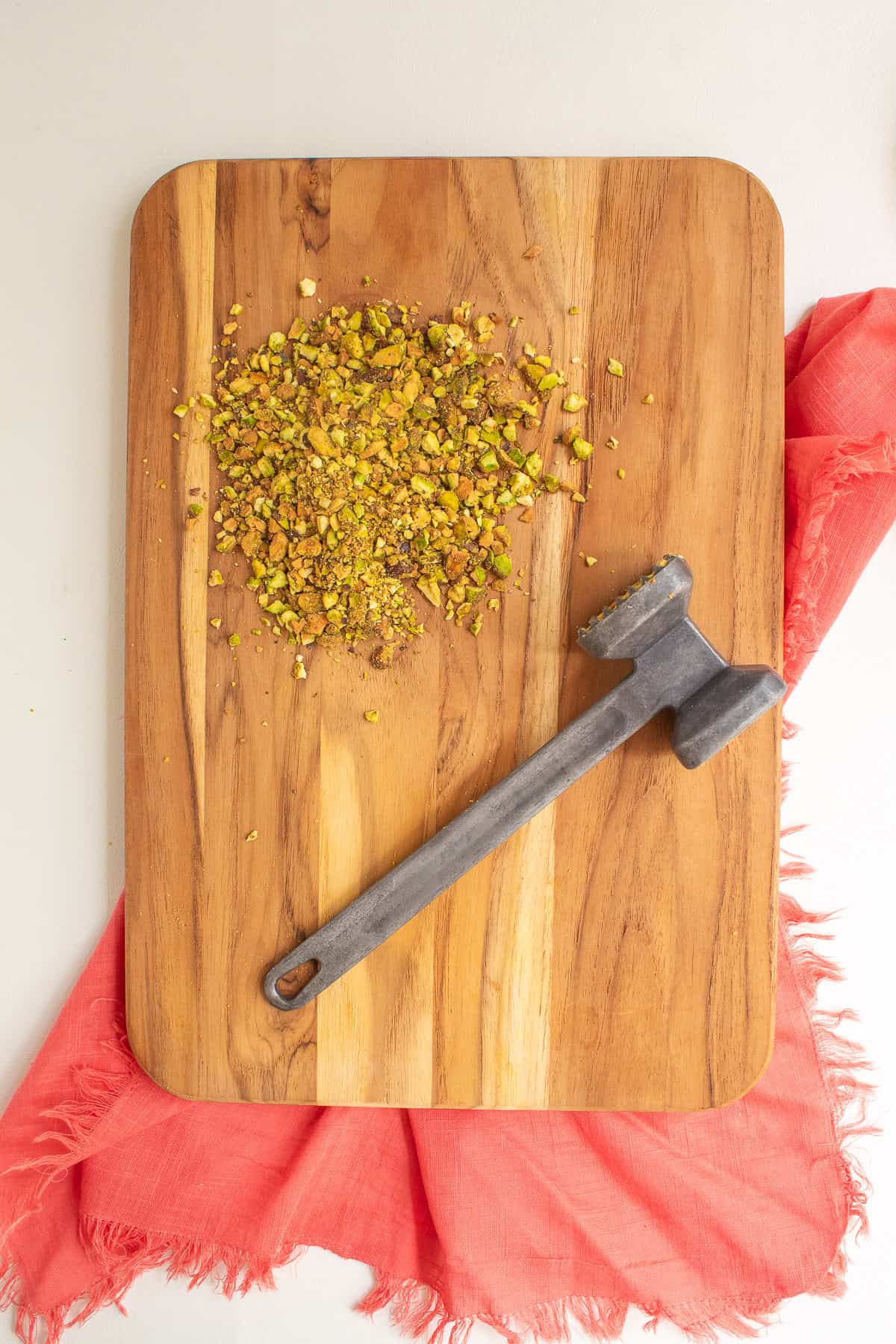 Pistachios are crushed with a mallet on a wooden cutting board.