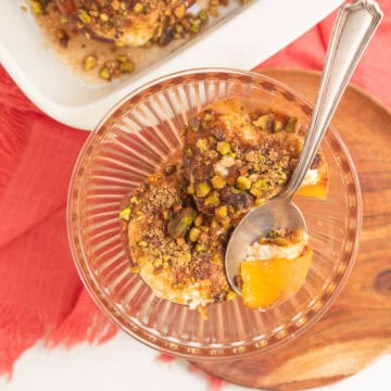 A spoonful of bright yellow peach with sour cream and a toasted pistachio mixture sits in a pale orange bowl.