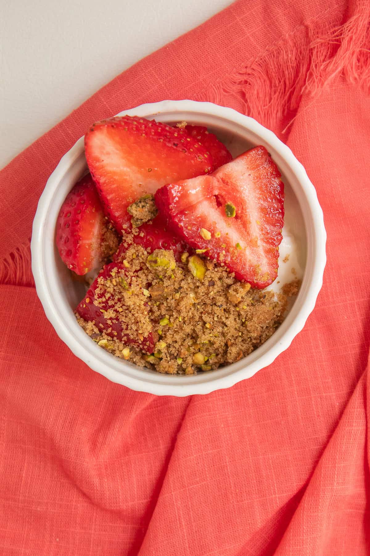 Extra pistachio mixture is sprinkled over strawberries and Greek yogurt in a small white bowl.