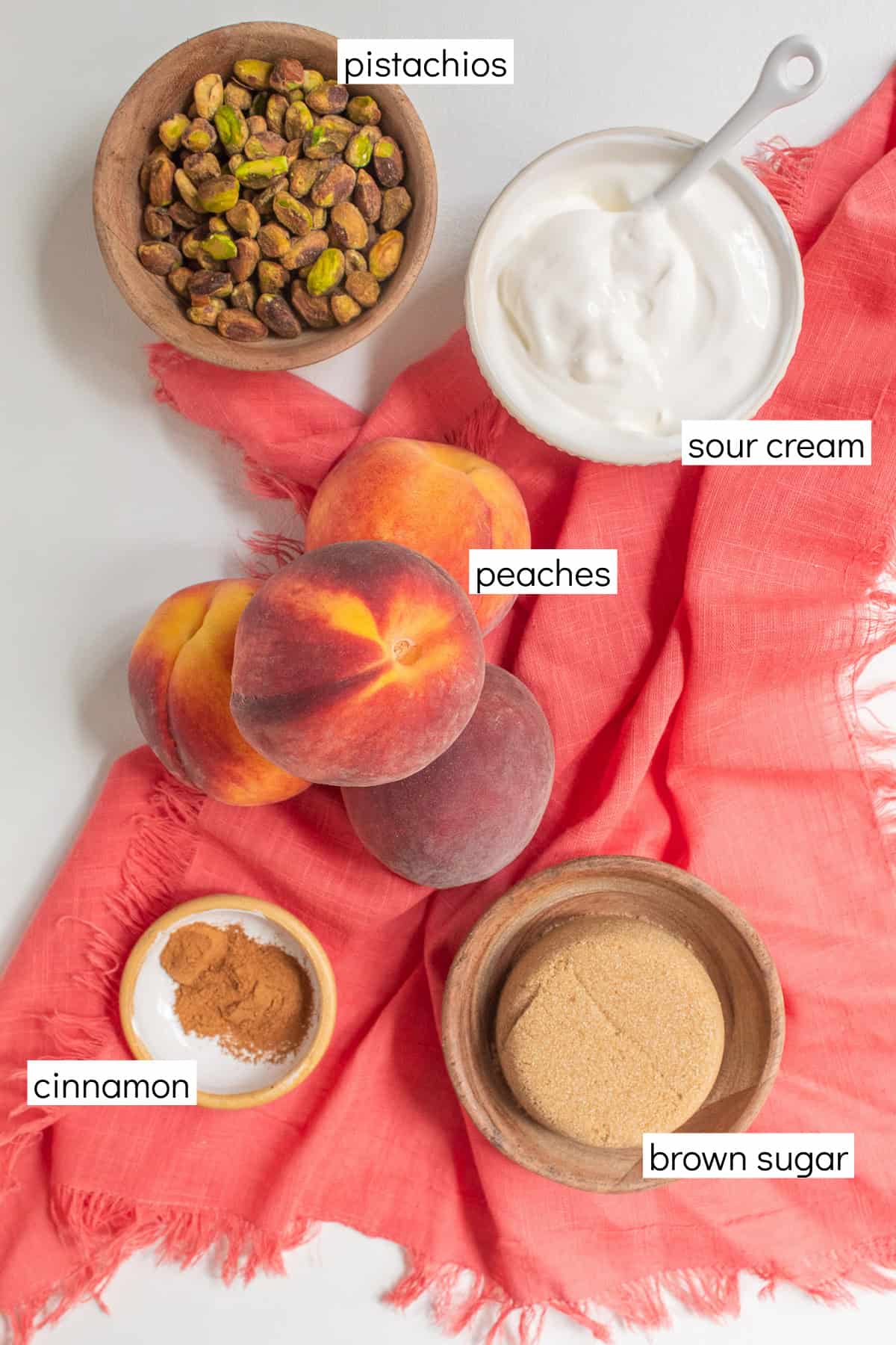 Ingredients for the recipe are displayed and labeled with white text boxes including the words pistachios, sour cream, peaches, cinnamon, and brown sugar.