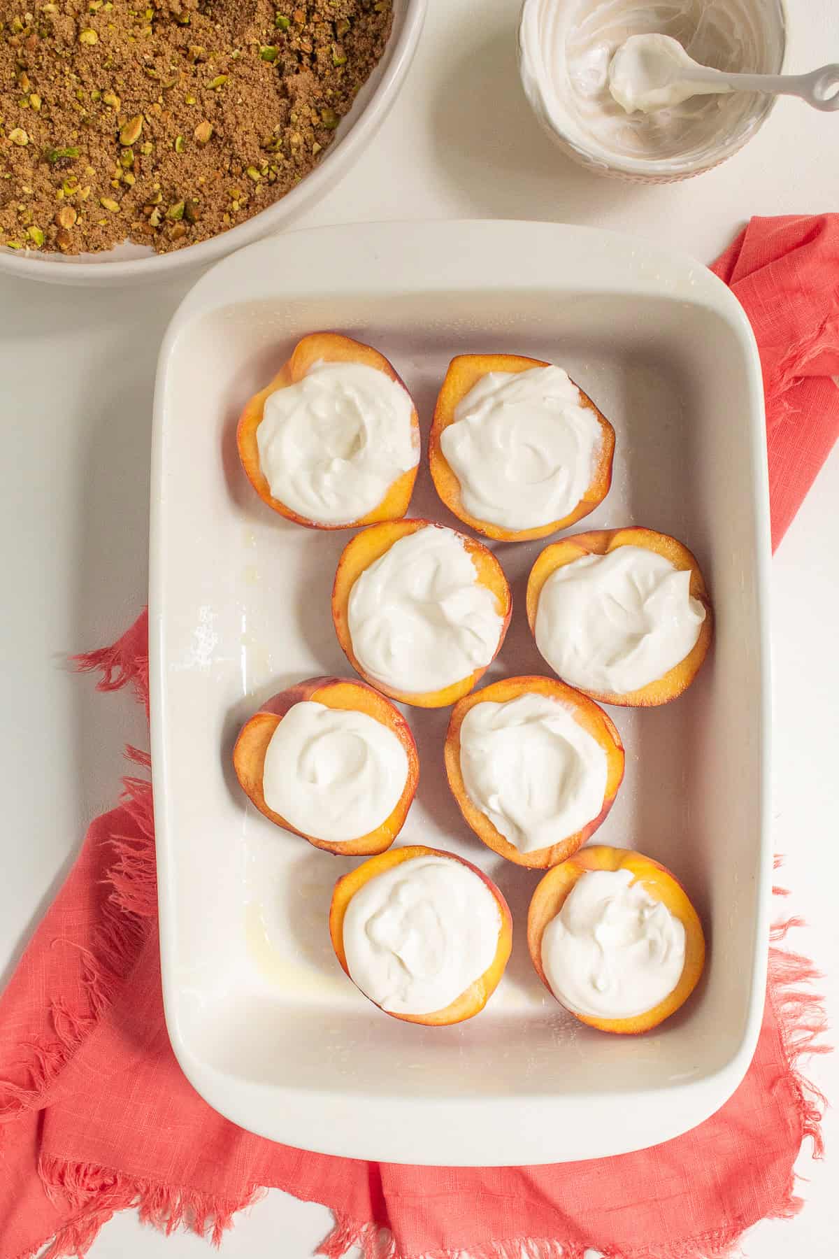 Peach halves are topped with sour cream in a white baking dish.