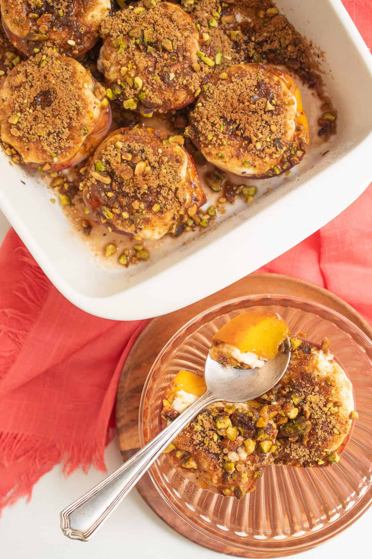 Bright yellow peach is topped with a layer of sour cream and toasted pistachio and brown sugar mixture in a fluted bowl next to a white baking dish.