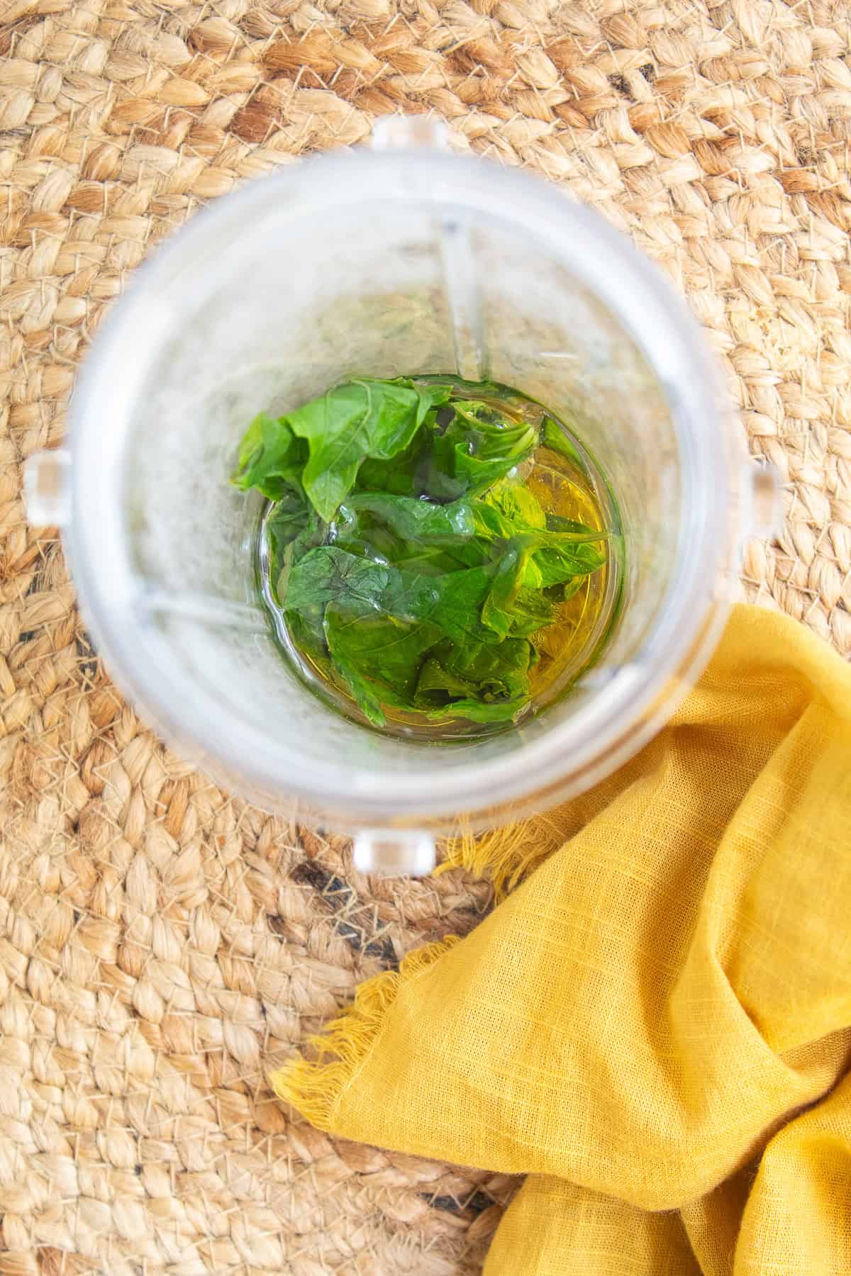 Blanched basil leaves are added to olive oil in a small blender.
