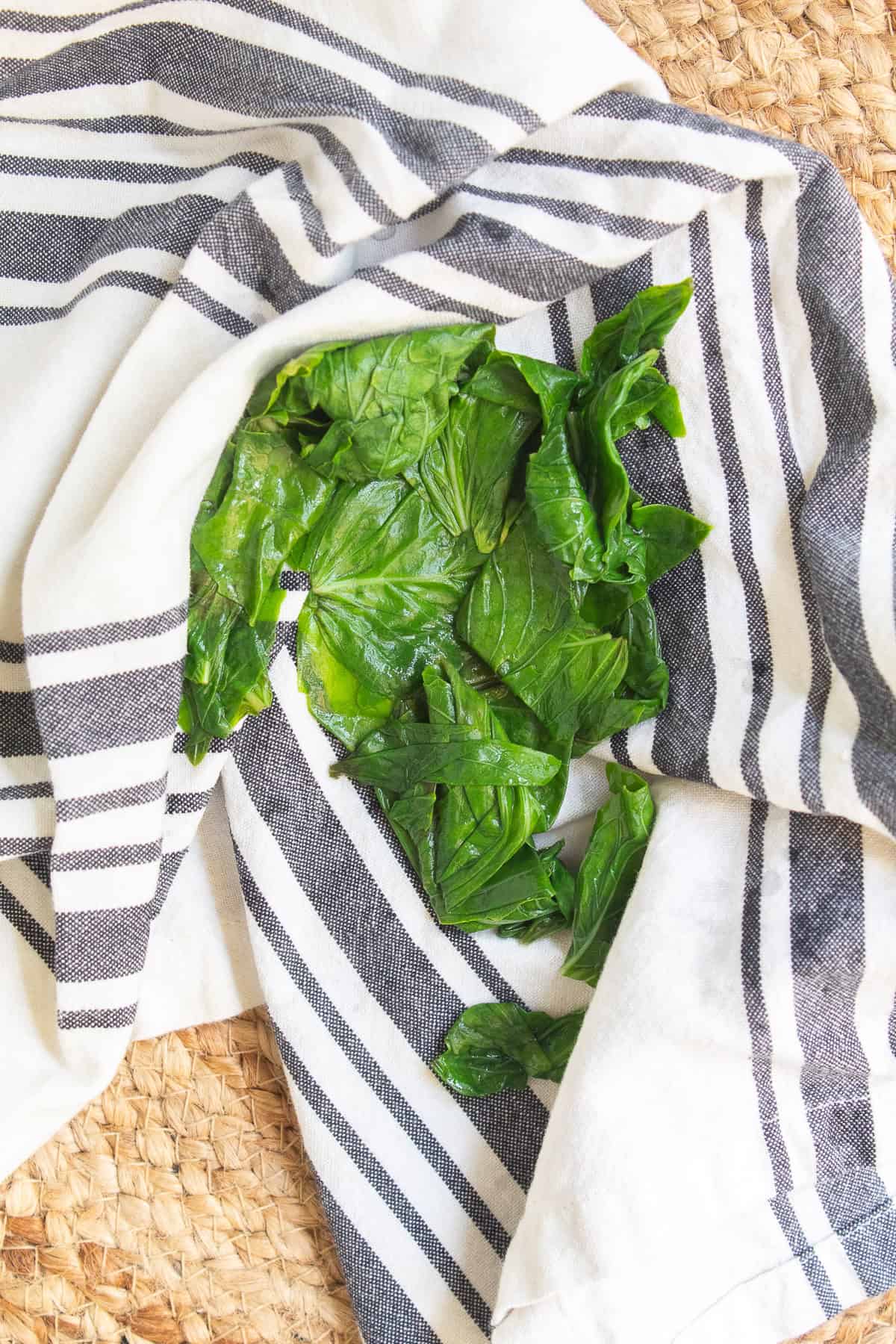 The cooled basil leaves are dried on a striped kitchen towel.