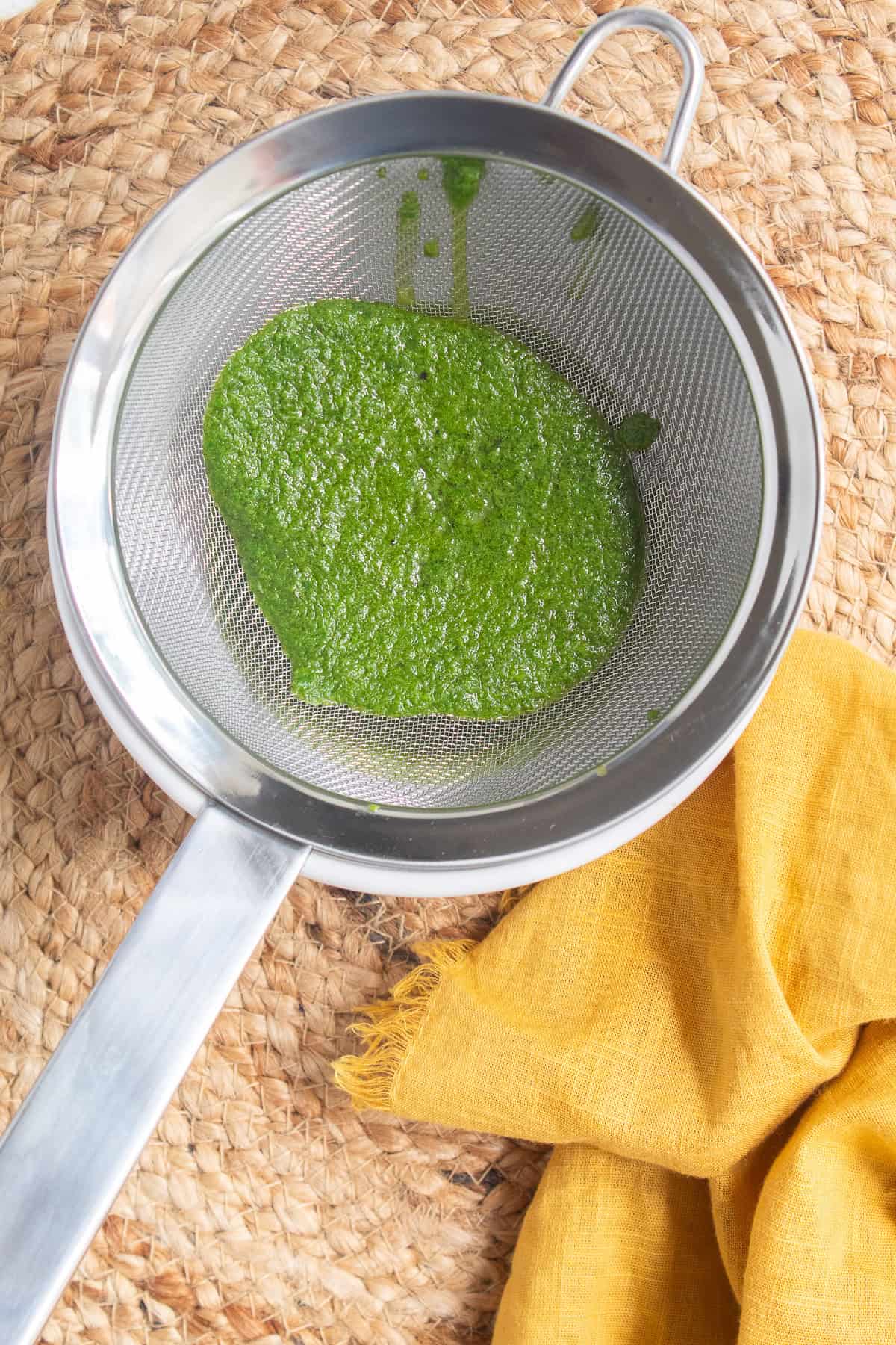 The blended basil and oil are strained over a wire mesh strainer.