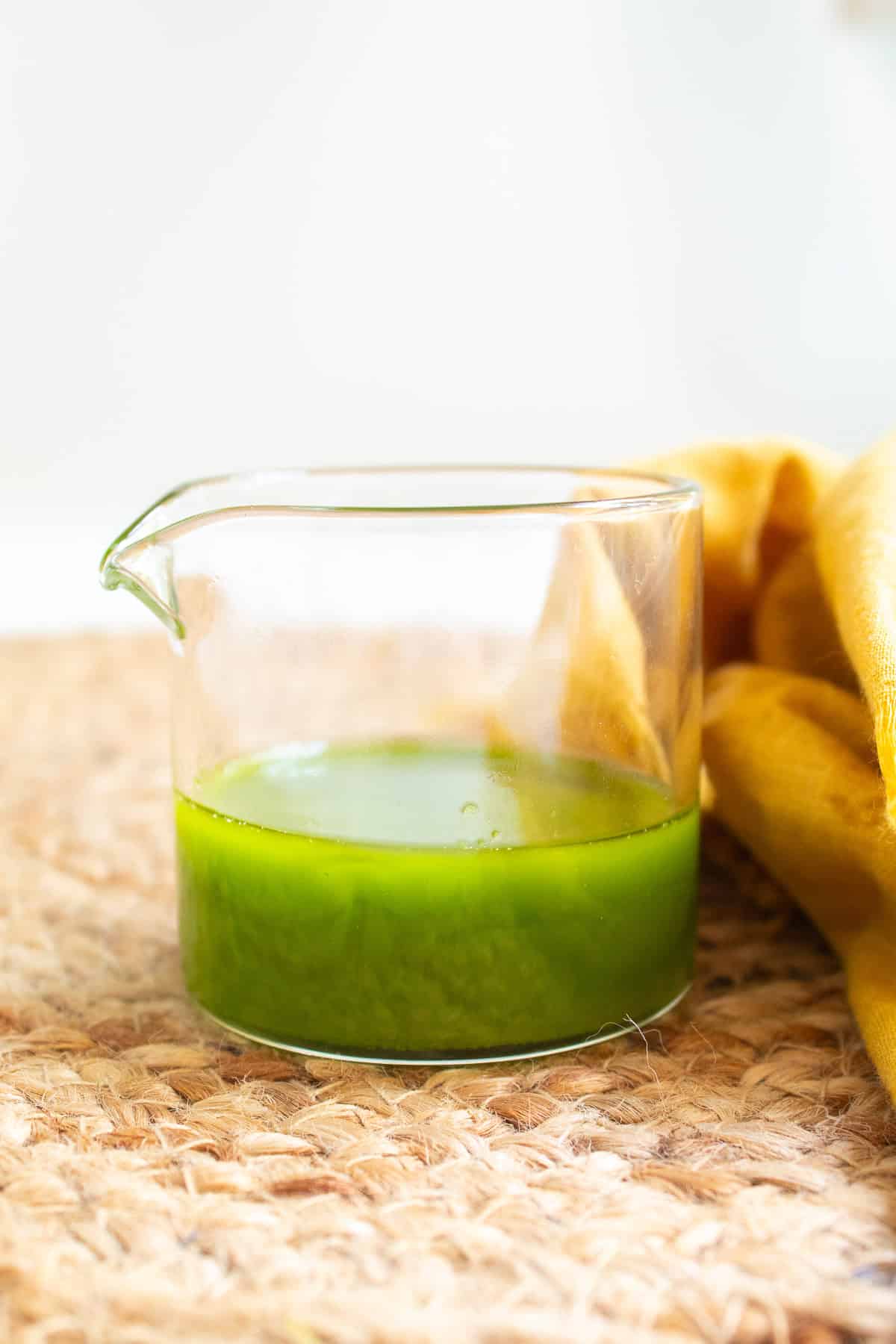 The basil oil is bright green in a small glass beaker.
