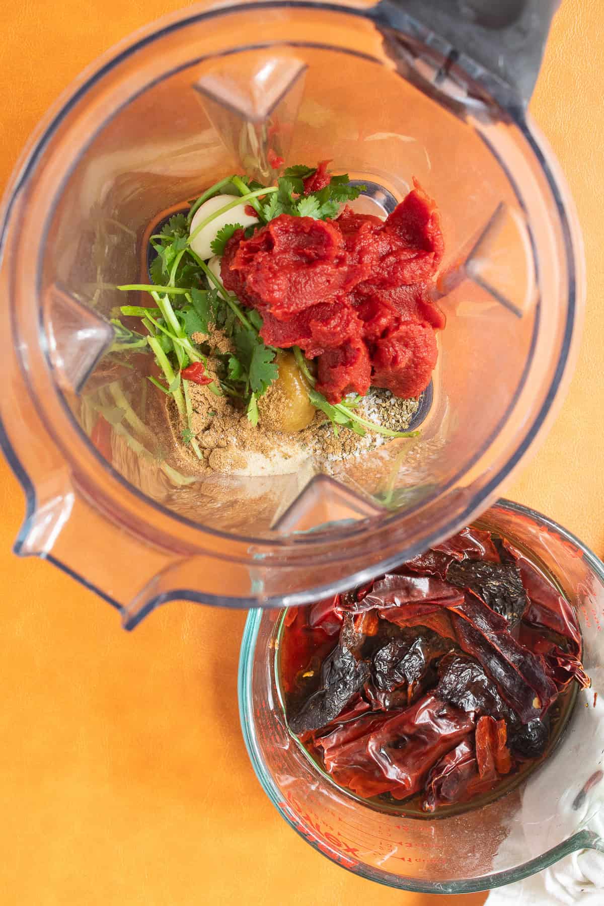 The soaked chiles are next to a blender containing cilantro, tomato paste, garlic, and spices.