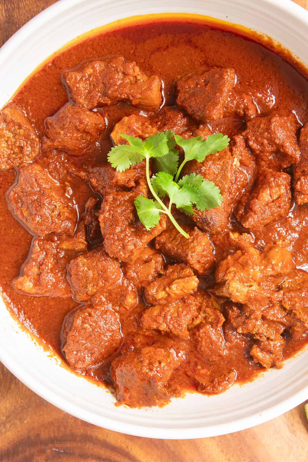 Tender chunks of pork are bathed in a rich red chile colorado sauce in a white bowl garnished with cilantro.