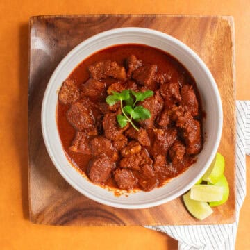 Tender chunks of pork are bathed in a rich red chile colorado sauce in a white bowl garnished with cilantro.