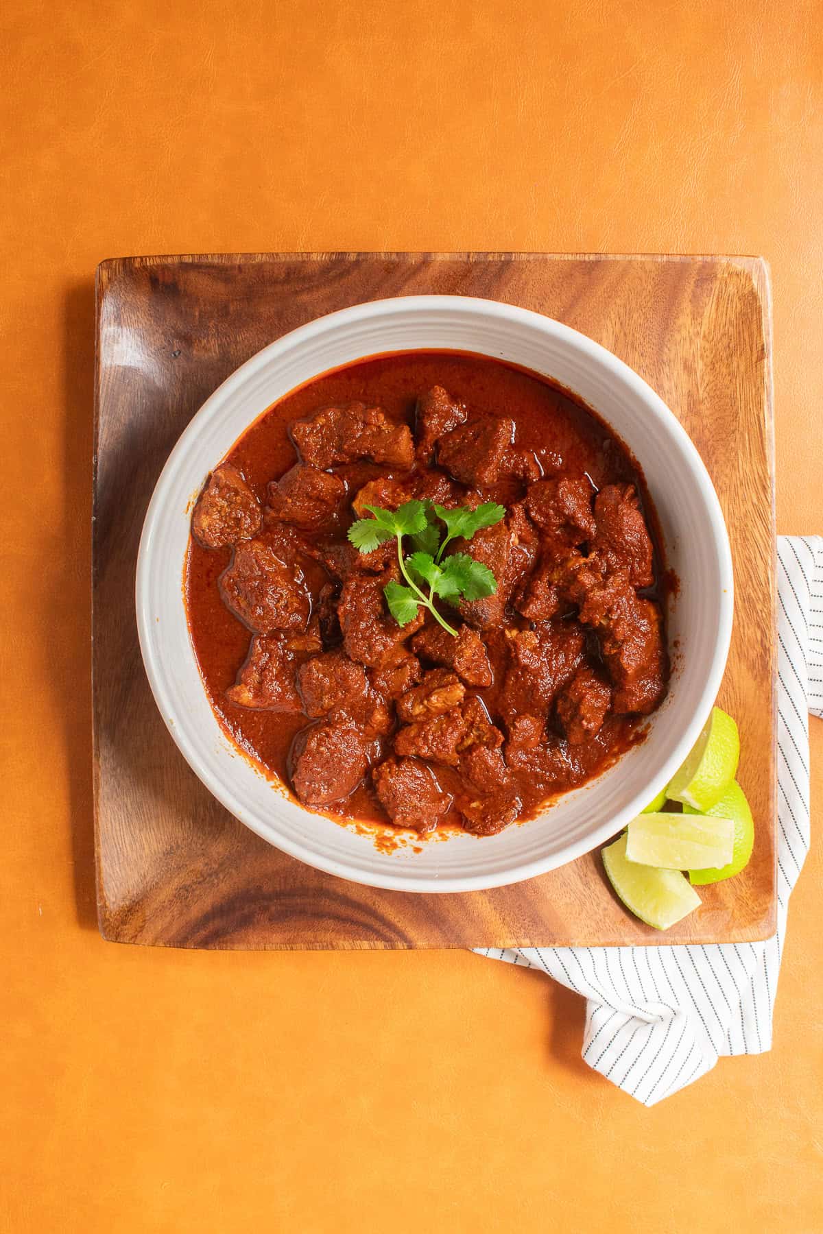 The chunks of pork in chile colorado sauce are served in a white bowl garnished with cilantro.