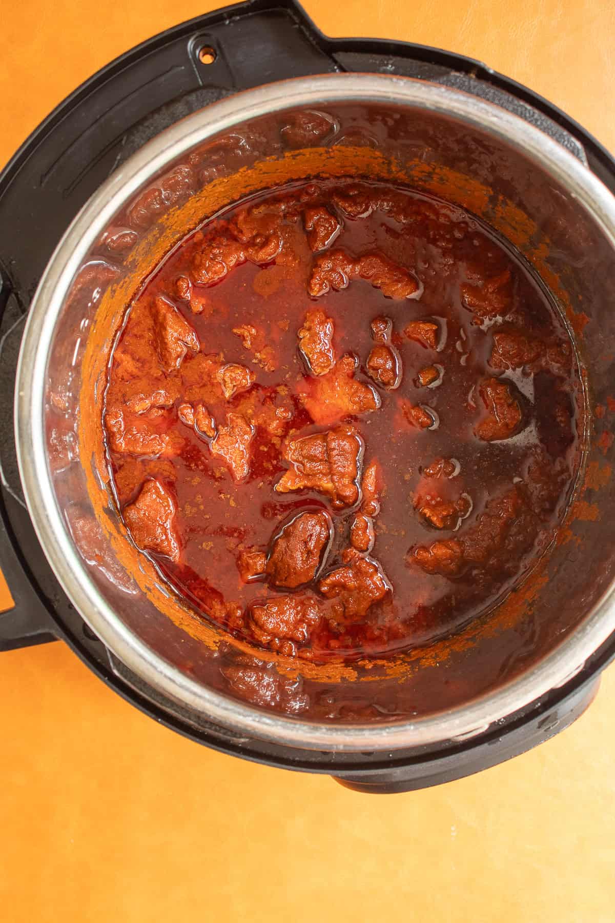 The cooked pork is bathed in a deep red sauce in the pressure cooker.