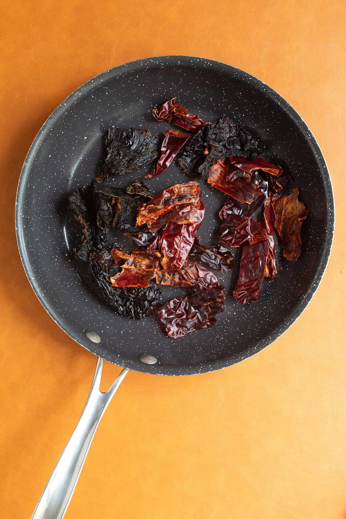 Dried chiles are added to a skillet for toasting.