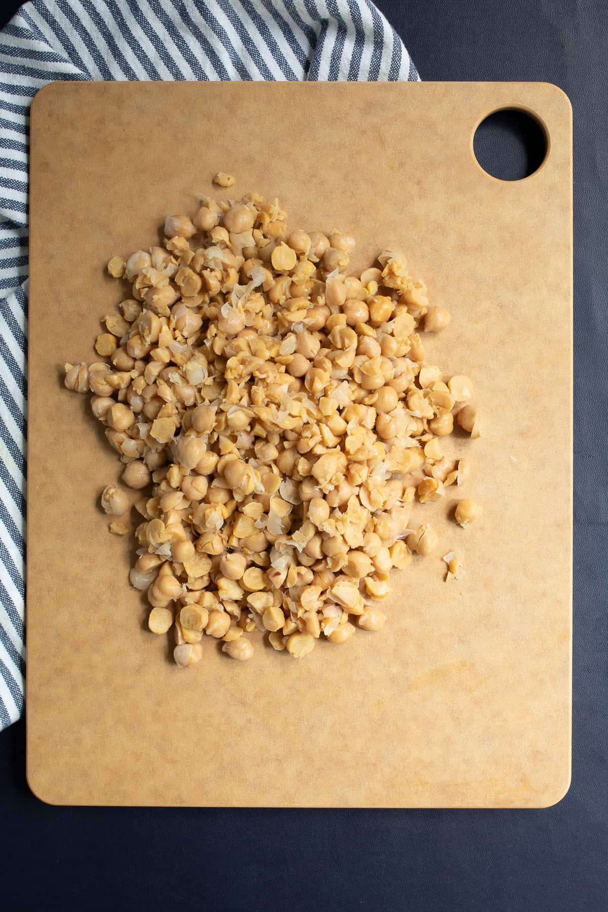 Garbanzo beans are roughly chopped on a brown cutting board.