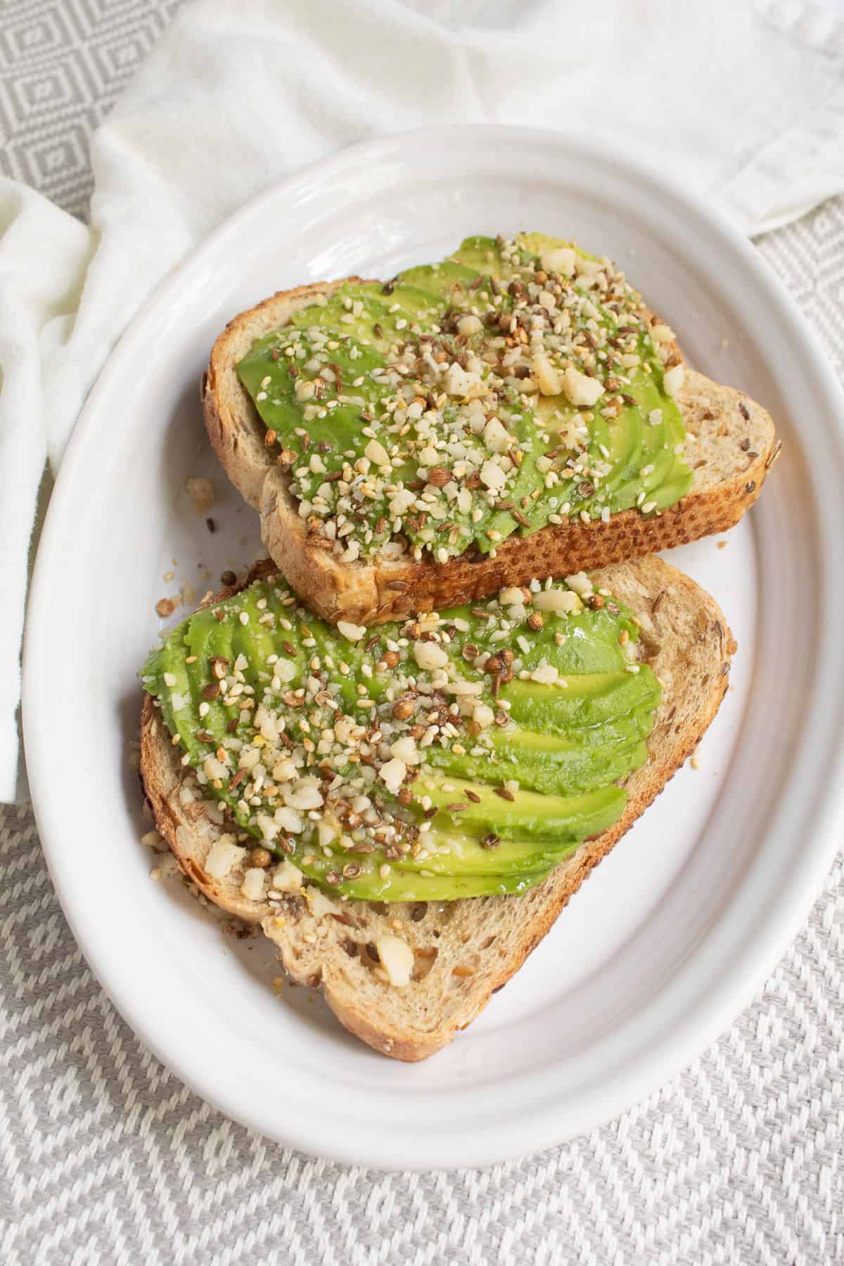 Dukkah is sprinkled over avocado toast and drizzled with olive oil.