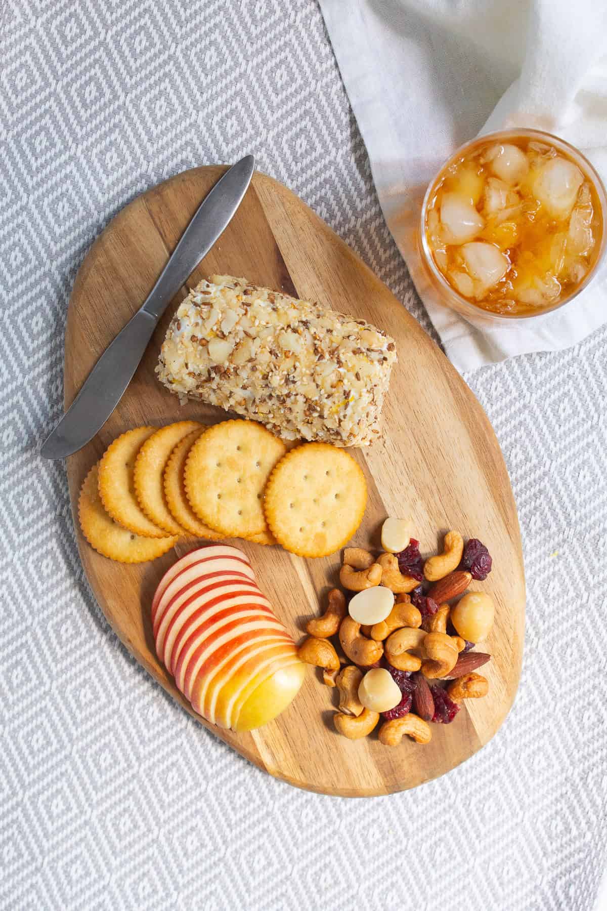 Goat cheese is pressed into a roll of goat cheese and served alongside crackers, nuts, and fruit and a cocktail.
