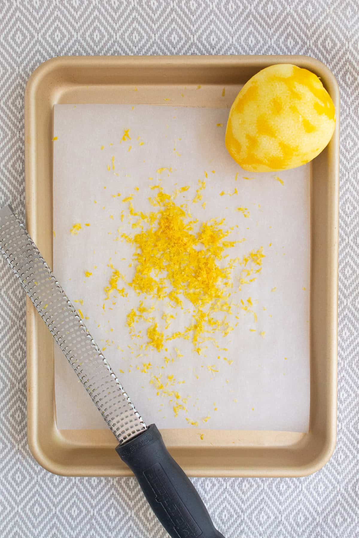 A lemon is zested over parchment paper lining a quarter sheet pan.