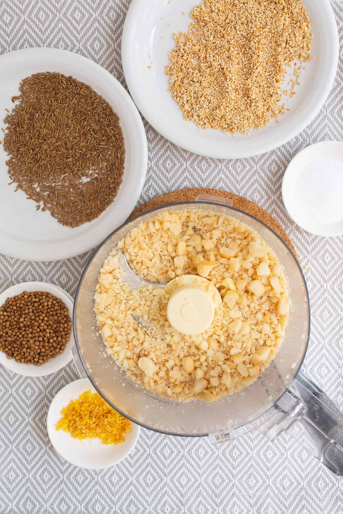 Macadamia nuts are crushed in the bowl of a food processor.