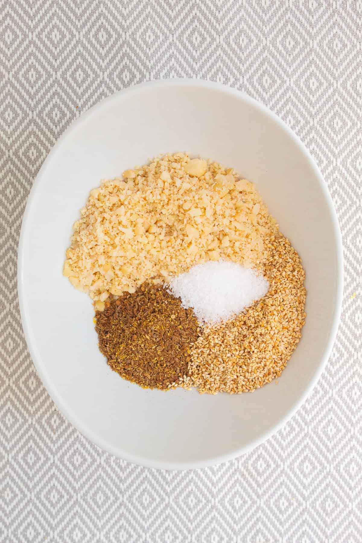 Ground and toasted seeds, lemon zest, salt, and macadamia buts are added to a medium bowl.