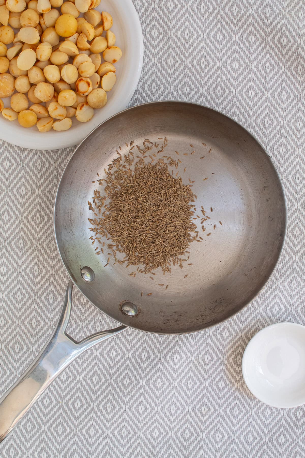 Cumin seeds are toasted in a small stainless skillet.