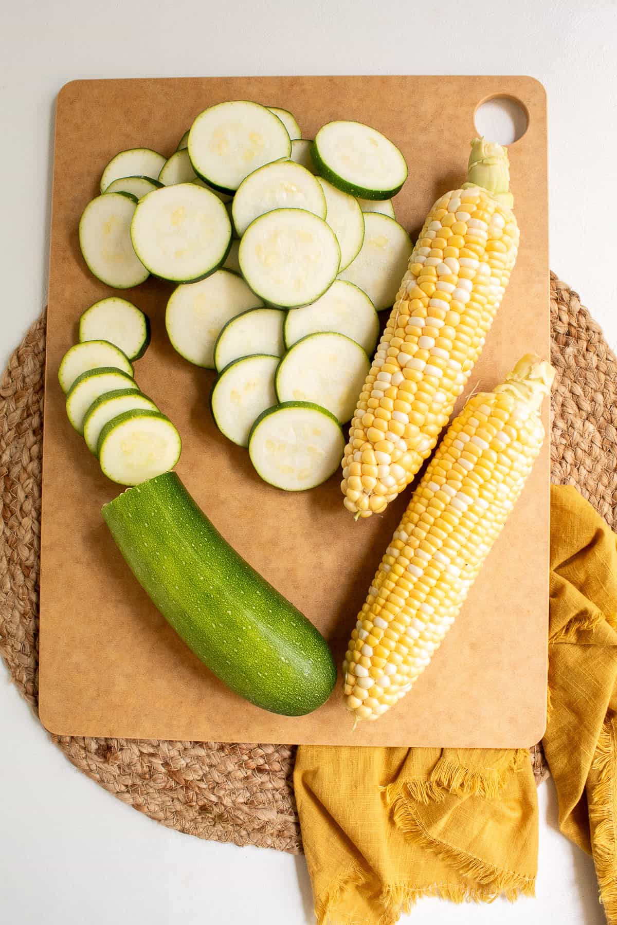 Zucchini is sliced and corn is cleaned before grilling.
