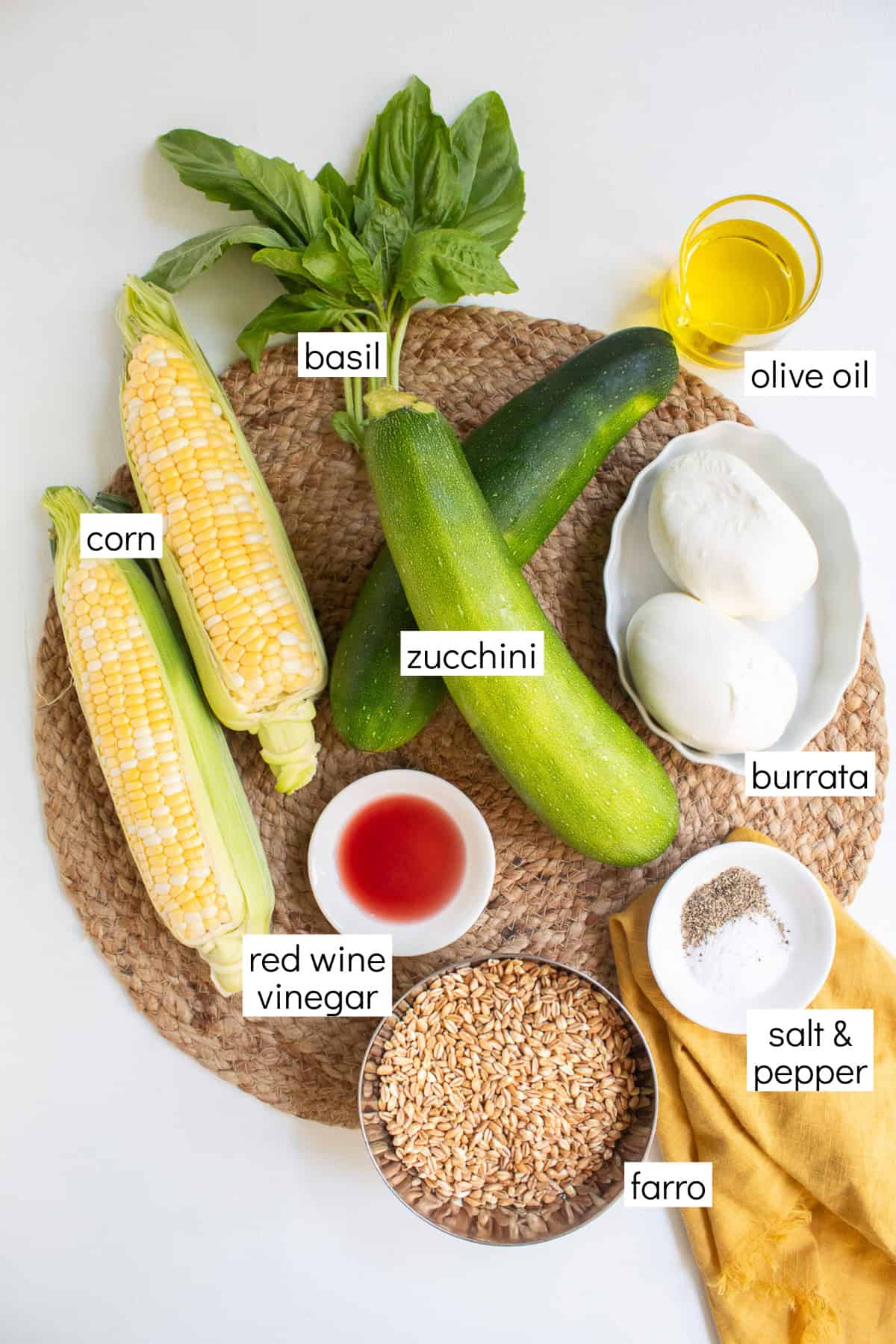 Ingredients for the recipe are displayed and labeled with white text boxes including the words corn, basil, olive oil, zucchini, burrata, red wine vinegar, salt & pepper, and farro.