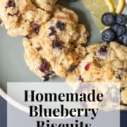 Biscuits are piled on a blue plate with lemon slices and fresh blueberries. A white text box at the bottom of the image contains the words, "homemade blueberry biscuits" and "plan. eat. post. repeat."
